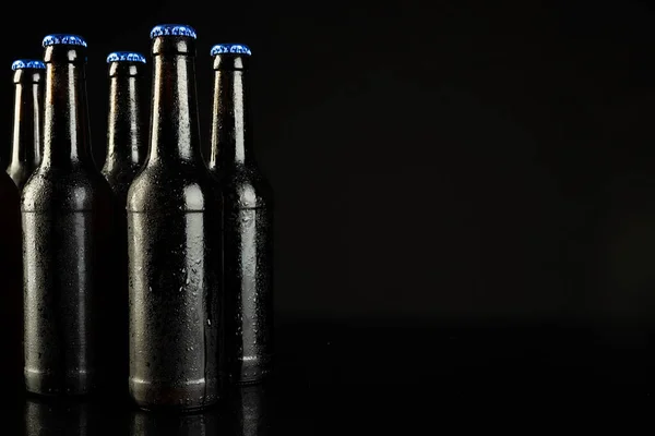 Image of five beer bottles with blue crown caps, with copy space on black background. Drinking alcohol, refreshment and lager day celebration concept.