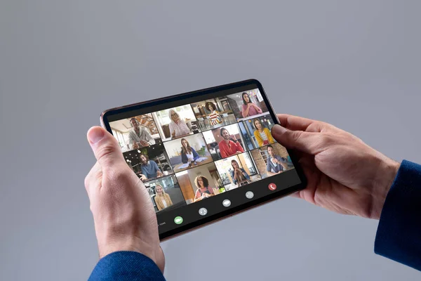 Hands of caucasian businessman making video call on tablet with diverse colleagues on screen. Business communication, flexible working and digital interface concept.