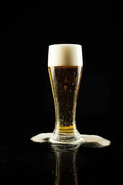 Image of overflowing pint glass of foamy beer, with copy space on black background. Drinking alcohol, refreshment and lager day celebration concept.