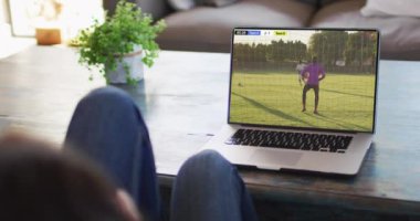 Farklı erkek futbol oyuncularının ekranda oynadığı dizüstü bilgisayar kullanan bir adam. Küresel spor kavramı, dijital kompozit video.