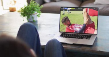 Farklı erkek futbol oyuncularının ekranda oynadığı dizüstü bilgisayar kullanan bir adam. Küresel spor kavramı, dijital kompozit video.