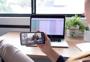 Kafkasyalı iş kadını akıllı telefon kullanarak masada oturuyor iş arkadaşlarıyla görüntülü görüşme yapıyor. Çevrimiçi toplantı, karantina süresince tecrit altında çalışma.