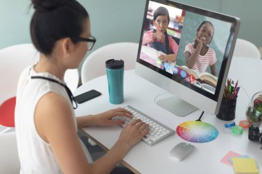 Beyaz kadın öğretmen okullu kızlarla video görüşmesinde bilgisayar kullanıyor. Çevrimiçi eğitim karantina süresince evde tek başına kalıyor..