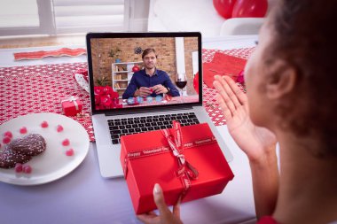 Çeşitli çiftler sevgililer günü videolarını dizüstü bilgisayarla çekiyor. Kadın elinde hediyelerle öpüşüyor. Karantina sırasında çevrimiçi sevgililer günü iletişimi. Çift