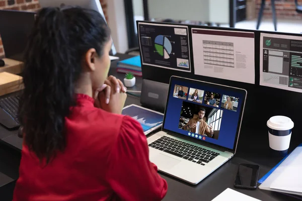 Caucasian woman in office having video call with diverse colleagues displayed on laptop screen. social distancing communication technology workplace during covid 19 pandemic.