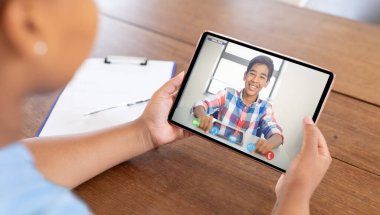 Karışık ırk işkadını masada oturup tablet kullanıyor ve video görüşmesi yapıyor. Modern bir ofiste çalışıyorum..