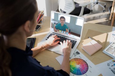 Beyaz kadın öğretmen okul çocuğuyla video görüşmesinde dizüstü bilgisayar kullanıyor. Çevrimiçi eğitim karantina süresince evde tek başına kalıyor.