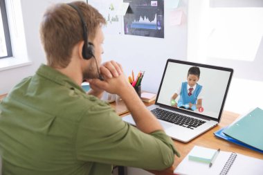 Erkek öğretmen kulaklık takıyor ve erkek öğrenciyle okulda video görüşmesi yapıyor. uzak öğrenim çevrimiçi eğitim kavramı
