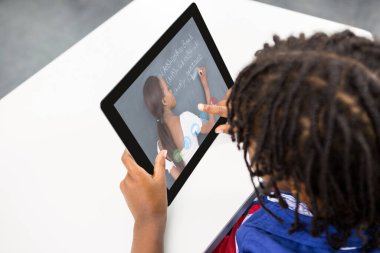 Bayan öğretmenle video görüşmesinde dijital tablet kullanan karışık ırk öğrencisi. Çevrimiçi eğitim karantina süresince evde tek başına kalıyor..