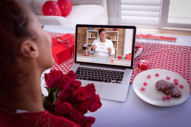Karışık ırktan bir kadın dizüstü bilgisayarında beyaz bir adamla sevgililer günü buluşması videosu çekiyor. Benimle evlen. Karantina süresince online öneri iletişimi.