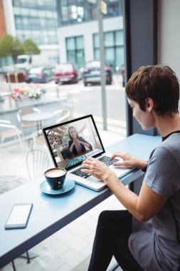 İş kadını ofiste dizüstü bilgisayar kullanırken kahve içiyor.