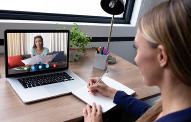 Masasında oturan beyaz bir kadın iş arkadaşıyla görüntülü görüşme yapıyor. Çevrimiçi toplantı, karantina süresince tecrit altında çalışma.