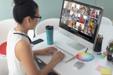 Asyalı iş kadını masa başında oturmuş bilgisayarla iş arkadaşlarıyla görüntülü konuşma yapıyor. Çevrimiçi toplantı, karantina süresince tecrit altında çalışma.