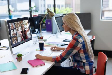 Beyaz bir kadın bilgisayar ekranında çeşitli meslektaşlarıyla görüntülü görüşme yapıyor. Covid 19 salgını sırasında sosyal mesafeli iletişim teknolojisi işyeri.