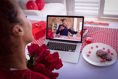 Güller tutan melez bir kadın sevgililer günü videosu çekiyor. Beyaz bir adamla dizüstü bilgisayar ekranında buluşuyor. Karantina süresince çevrimiçi sevgililer günü iletişimi.