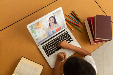 Bayan öğretmenle video görüşmesinde bilgisayar kullanan karışık ırk öğrencisi. Çevrimiçi eğitim karantina süresince evde tek başına kalıyor..