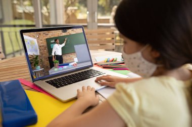 Yüz maskesi takan kız öğrenci, erkek öğretmenle okulda video görüşmesi yapıyor. covid-19 konsepti sırasında uzak öğrenim çevrimiçi eğitim