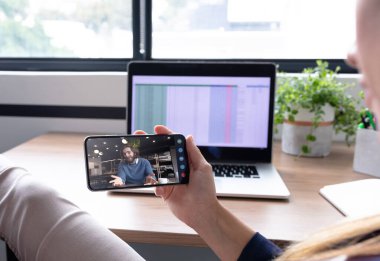 Beyaz kadın akıllı telefon kullanıyor ve iş arkadaşıyla görüntülü görüşme yapıyor. Çevrimiçi toplantı, karantina süresince tecrit altında çalışma.