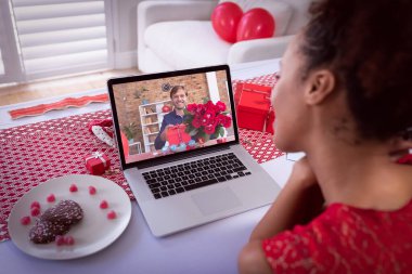 Sevgililer Günü videosu çeken çeşitli çiftler elinde çiçek ve hediyeyle dizüstü bilgisayardaki adamı arıyor. Karantina süresince çevrimiçi sevgililer günü iletişimi.
