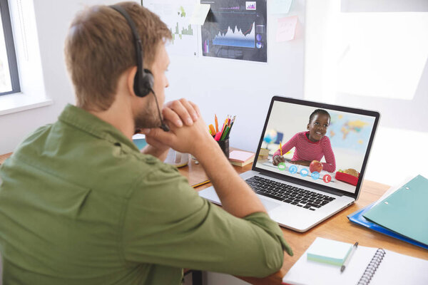 Male teacher wearing headphones having a video call with female student on laptop at school. distance learning online education concept