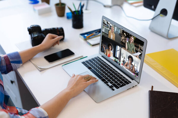 Caucasian woman in office having video call with diverse colleagues displayed on laptop screen. social distancing communication technology workplace during covid 19 pandemic.