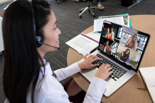 Caucasian woman in office having video call with diverse colleagues displayed on laptop screen. social distancing communication technology workplace during covid 19 pandemic.