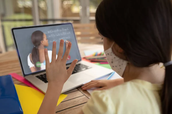 白人女学生戴着面具 与女教师在手提电脑视频通话中挥手 在隔离隔离期间 在线教育在家中自我隔离 — 图库照片