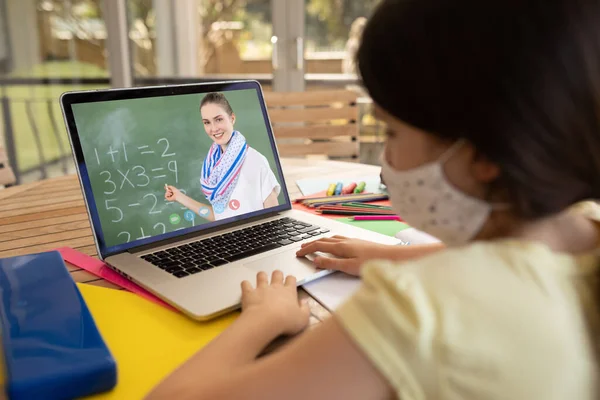 在学校 戴着面具的女学生在笔记本电脑上与女教师进行视频通话 Covid 19概念期间的在线远程教育 — 图库照片