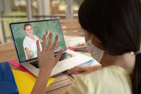 白人女学生戴着面具 与女教师在手提电脑视频通话中挥手 在隔离隔离期间 在线教育在家中自我隔离 — 图库照片