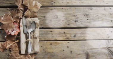 Çatal bıçak takımının üzerindeki ışık lekeleri ve tahta arka plandaki yapraklar. Sonbahar geleneği ve kutlama konsepti dijital olarak oluşturuldu.