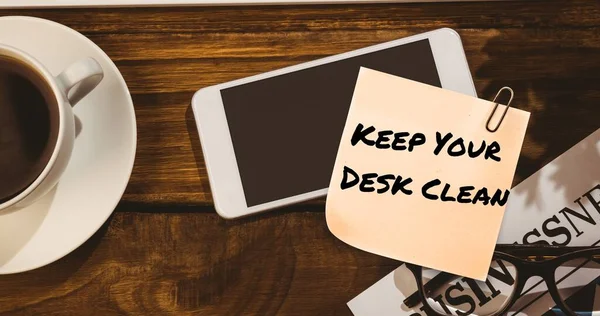 Composite of keep your desk clean on sticky note with cellphone and coffee on table. Office, drink, beverage, hygiene, awareness, celebration and technology concept.