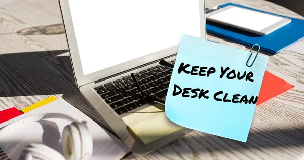 Composite of keep your desk clean text on sticky note with laptop and office supplies on table. Office, desk, stationery, hygiene, awareness, celebration and technology concept.