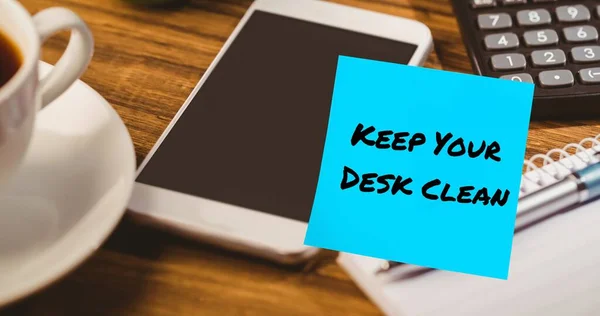 Composite of keep your desk clean text on blue sticky note with cellphone, calculator and coffee. Office, table, drink, copy space, stationery, hygiene, awareness, celebration and technology.