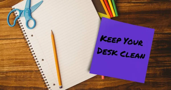Composite of keep your desk clean on sticky note with pencil, scissors and notebook on table. Office, stationery, hygiene, awareness, celebration and technology concept.
