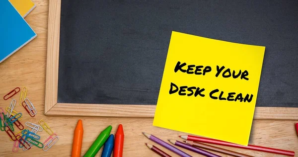 Composite of keep your desk clean text on sticky note with slate and colored pencils. Office, desk, copy space, stationery, hygiene, awareness, celebration and creativity concept.