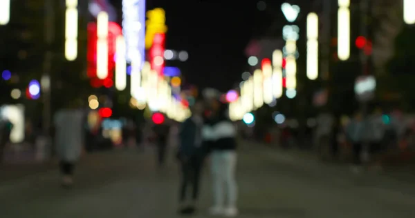 Image of defocussed shop and street lights, with people walking on a city road at night. City life, nightlife, electricity and travel concept.