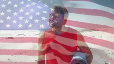 Amerika Birleşik Devletleri bayrağının animasyonu ve plajda yoga minderiyle kıdemli melez adam. Amerikan vatanseverliği, çeşitlilik ve gelenek konsepti dijital olarak oluşturulmuş video.