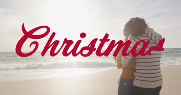 ビーチでの出産のカップルの上にクリスマスのテキストのアニメーション クリスマス お祝いのコンセプトデジタル生成ビデオ — ストック動画