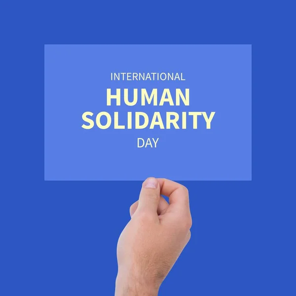 Composition of hand holding blue board with international human solidarity day text. Human solidarity, helping and empathy concept.