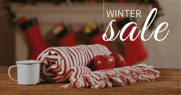 Composition of winter sale text over winter blanket with apples and mug in background. Christmas, sales, tradition, celebration and festivity concept digitally generated image.
