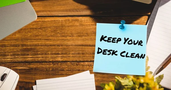Composite of keep your desk clean text on sticky note with office supplies on wooden table. Office, stationery, hygiene, awareness, celebration concept.