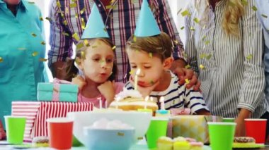 Kafkas erkek ve kız üzerinde konfeti animasyonu pastaya mum üflüyor ve evde ebeveynler var. Dijital kompozit, çocukluk, birliktelik, aile, arkadaşlık, doğum günü ve kutlama konsepti.