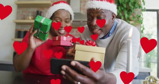 Animación Corazones Rojos Sobre Pareja Afroamericana Sombreros Santa Con Smartphone — Vídeos de Stock