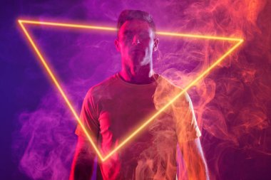 Beyaz tenli erkek oyuncu ışıklı üçgenle neon arka planda duruyor, kopyalama alanı. Dijital kompozit, spor, futbol, rekabet, neon, parıltı, duman ve soyut kavram.