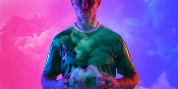 男子高加索足球运动员拿着球站着 烟雾腾腾的粉色和蓝色背景 复制空间 数字合成 霓虹灯和抽象概念 — 图库照片