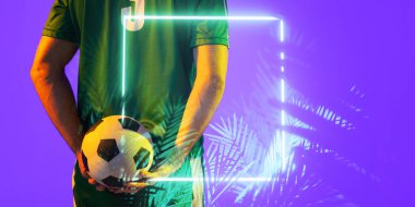 Beyaz tenli erkek oyuncunun, aydınlanmış dikdörtgen ve bitkilerin üzerinde topu tutuşu, kopyalama alanı. Dijital kompozit, mor, spor, futbol, rekabet, neon, parlayan ve soyut kavram.