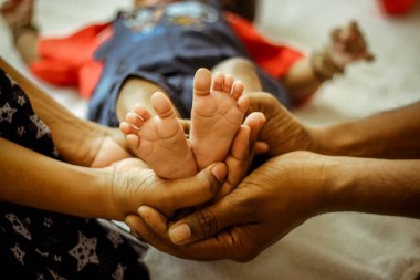 Parenthood Concept - Happy Mom and Dad are holding Baby feet on hands. Parents are holding the legs of a newborn baby