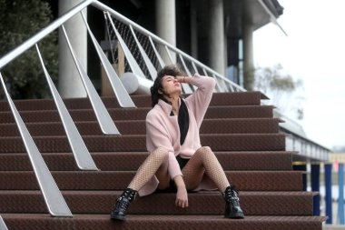 Şehrin merdivenlerinde oturan genç bir kadın elinde file çorapla poz veriyor. Şehir modası