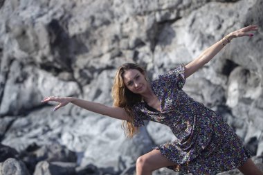 Genç, güzel balerin dans ediyor, sahilde taş üstünde poz veriyor.