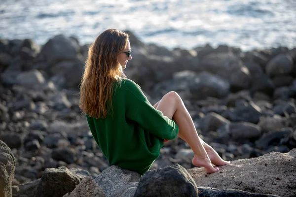 Uzun Saçlı Model Kayalık Bir Plajda Oturuyor Yeşil Kazaklı Uzun — Stok fotoğraf